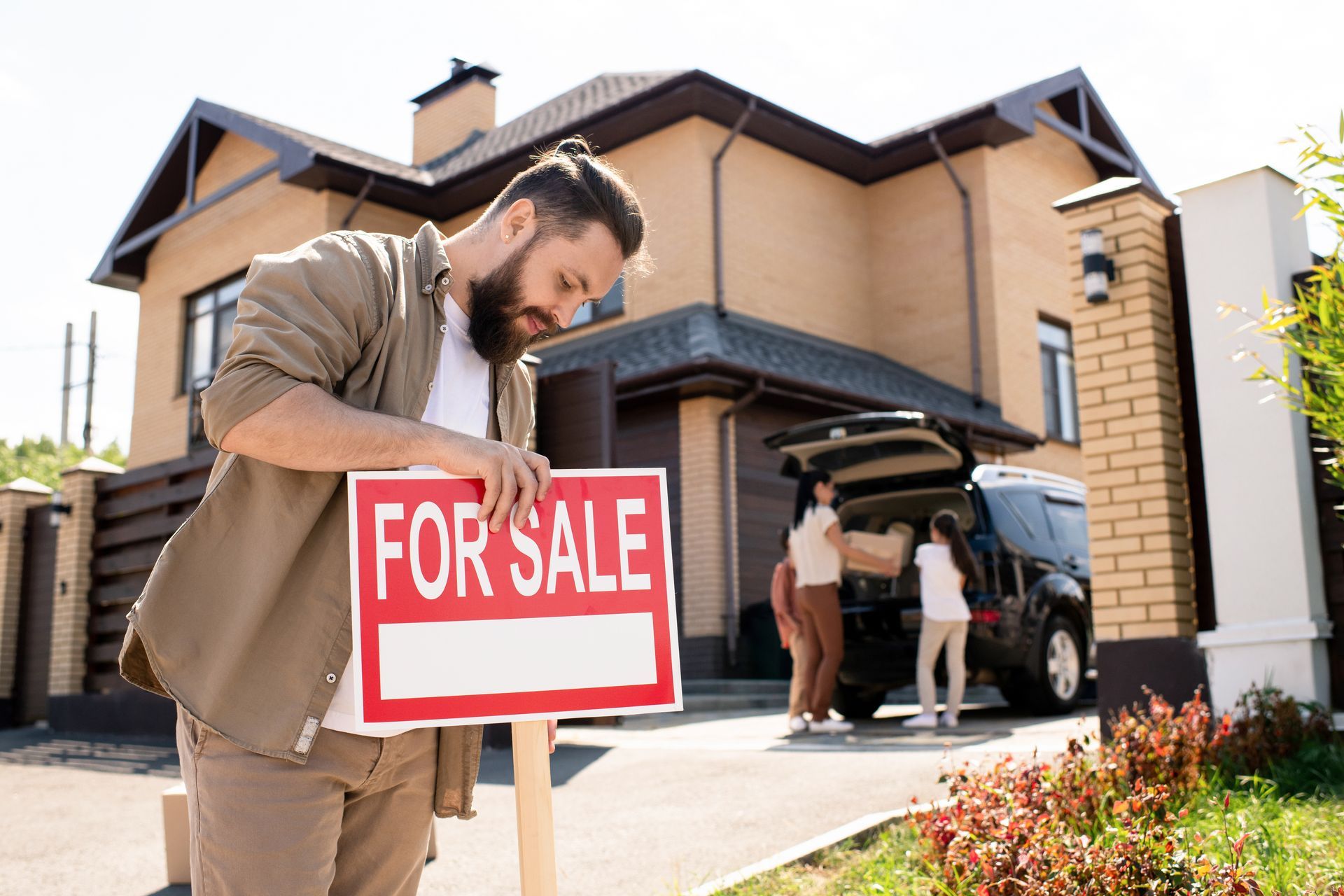 A man pulls up a for sale sign in front of a house.