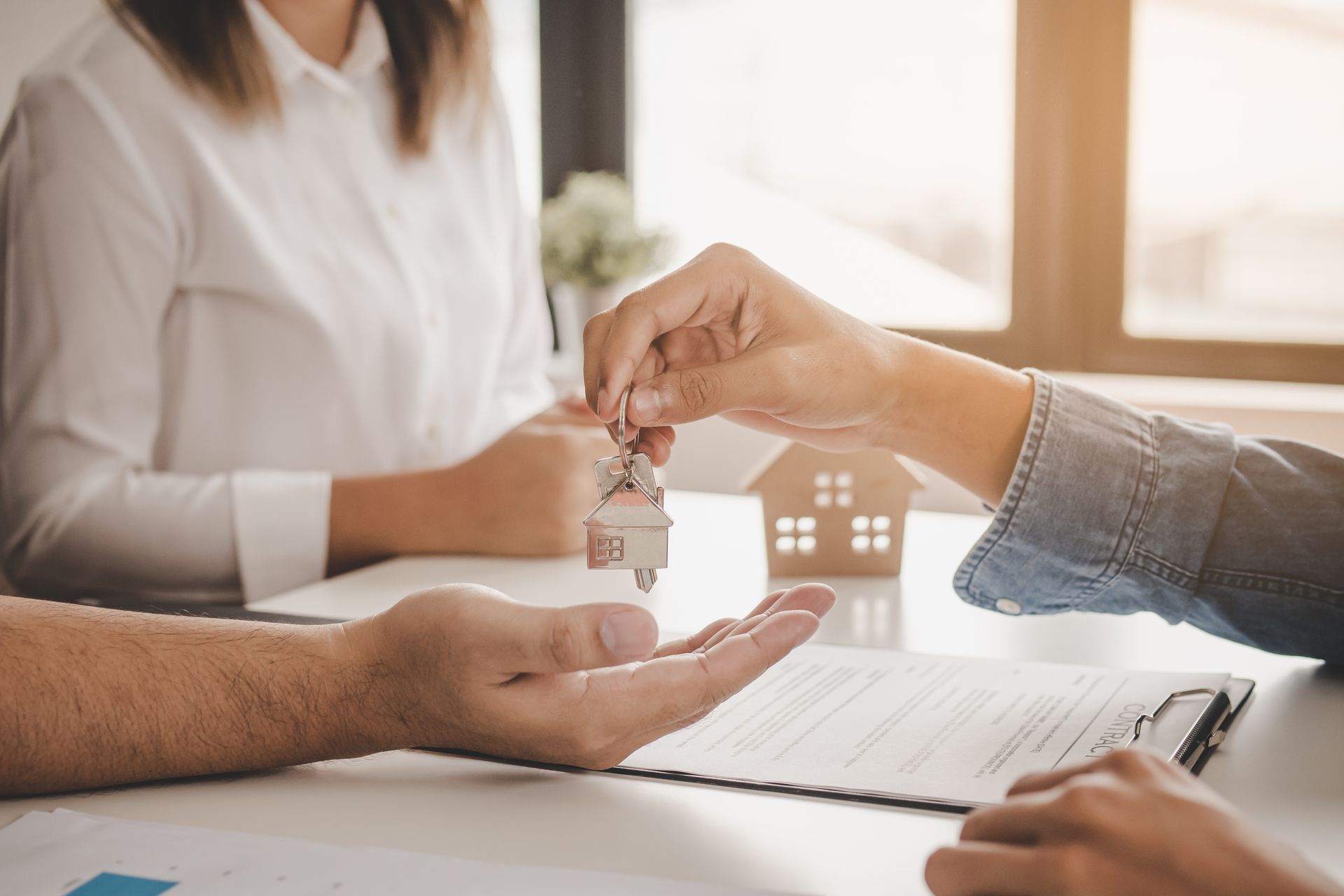 A hand passes house keys to another person during a real estate signing at a desk. A hand passes house keys to another person during a real estate signing at a desk.