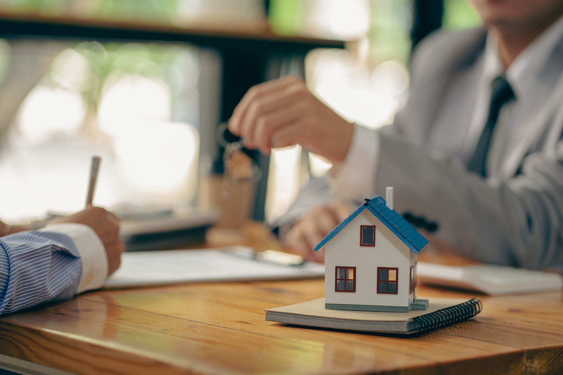 Small house model on a desk during a real estate meeting with two people in the background