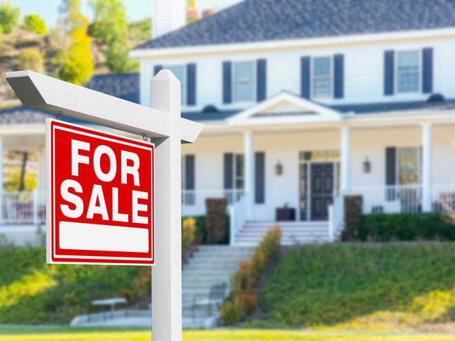 A for sale sign in front of a large white house. For sale sign in front of a white suburban house with a porch and steps