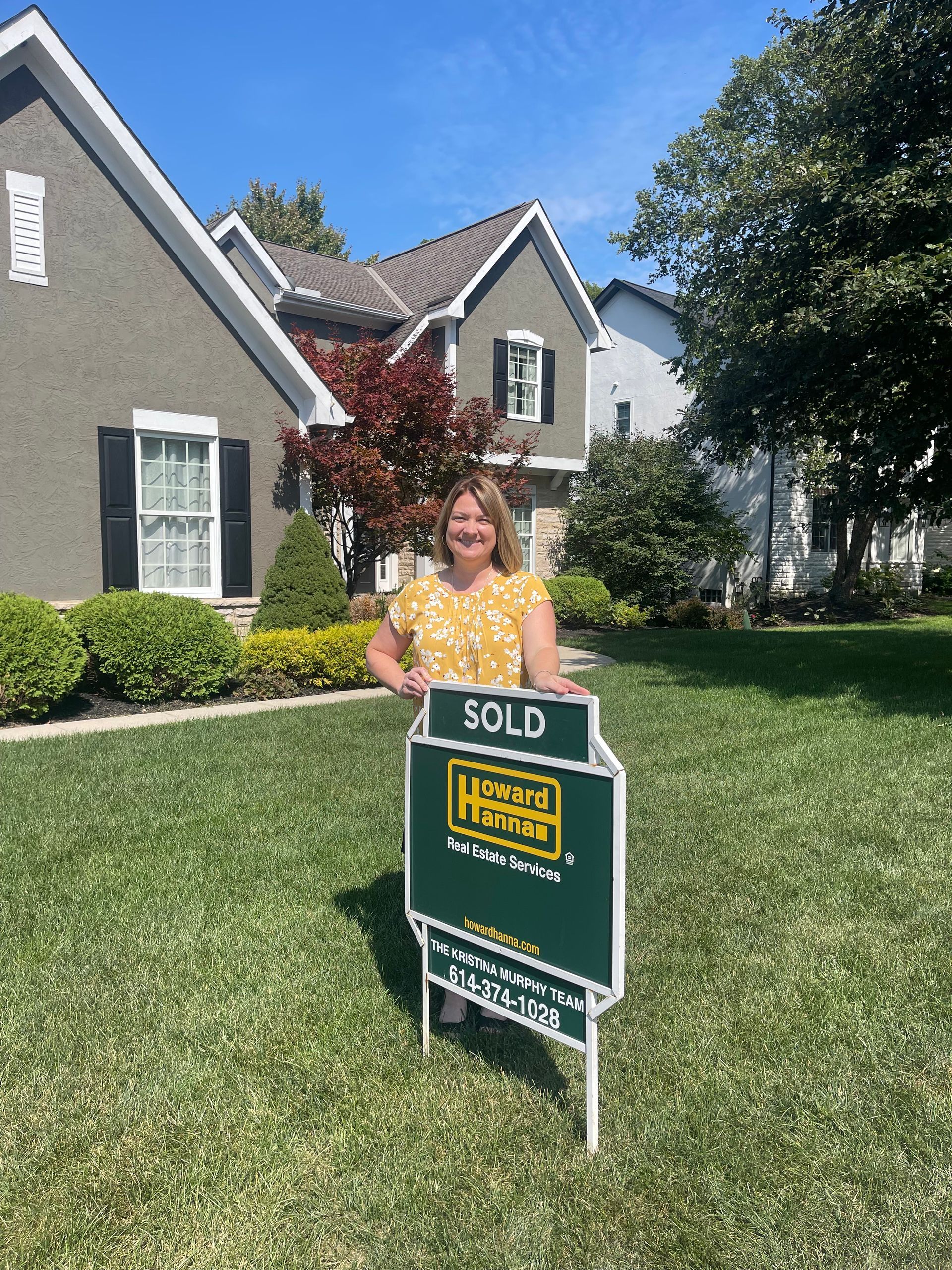 Woman holding a SOLD real estate sign in front of a suburban house and lawn