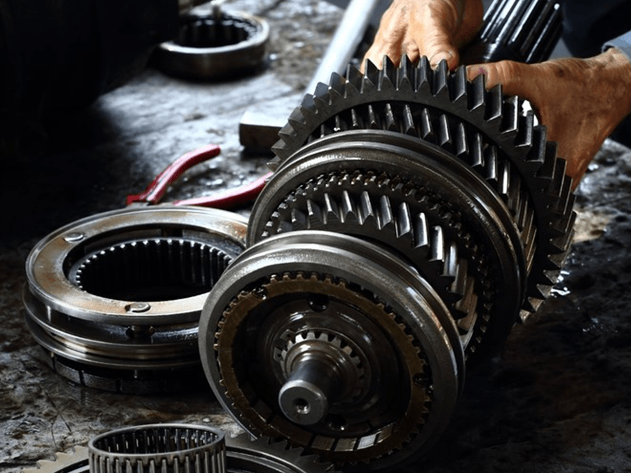 Hands working on a large metal gear assembly on a workshop floor