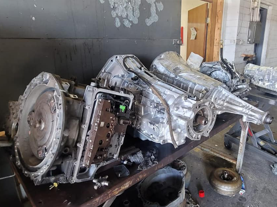 Damaged silver car transmission assembly on a workbench in a garage, with parts and tools nearby