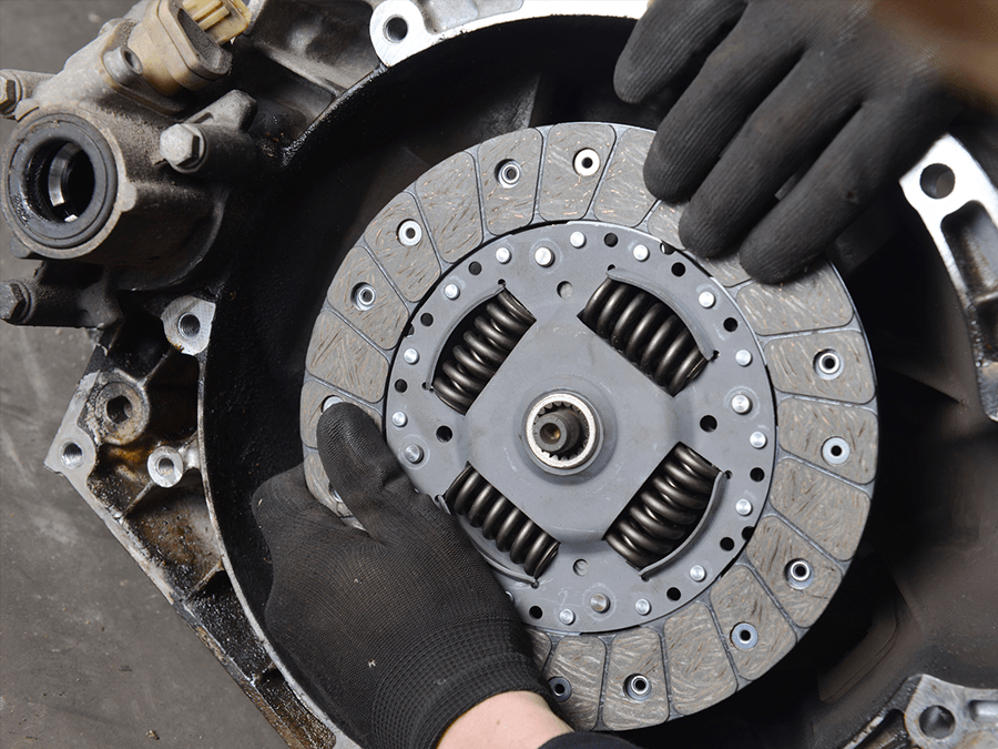 Gloved hands installing a car clutch disc inside an engine assembly
