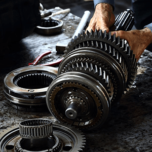 Hands assembling a metal gear transmission on a workbench in a dim workshop