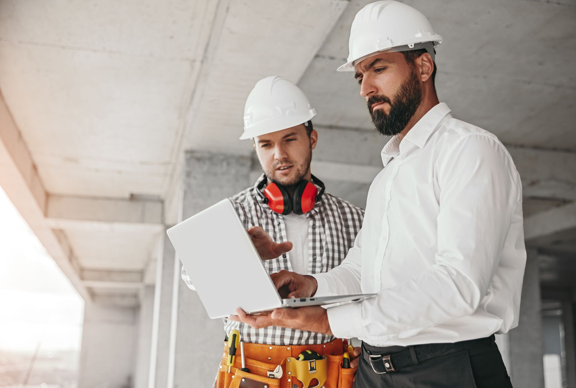 Two construction workers in hard hats review a clipboard at a building site.