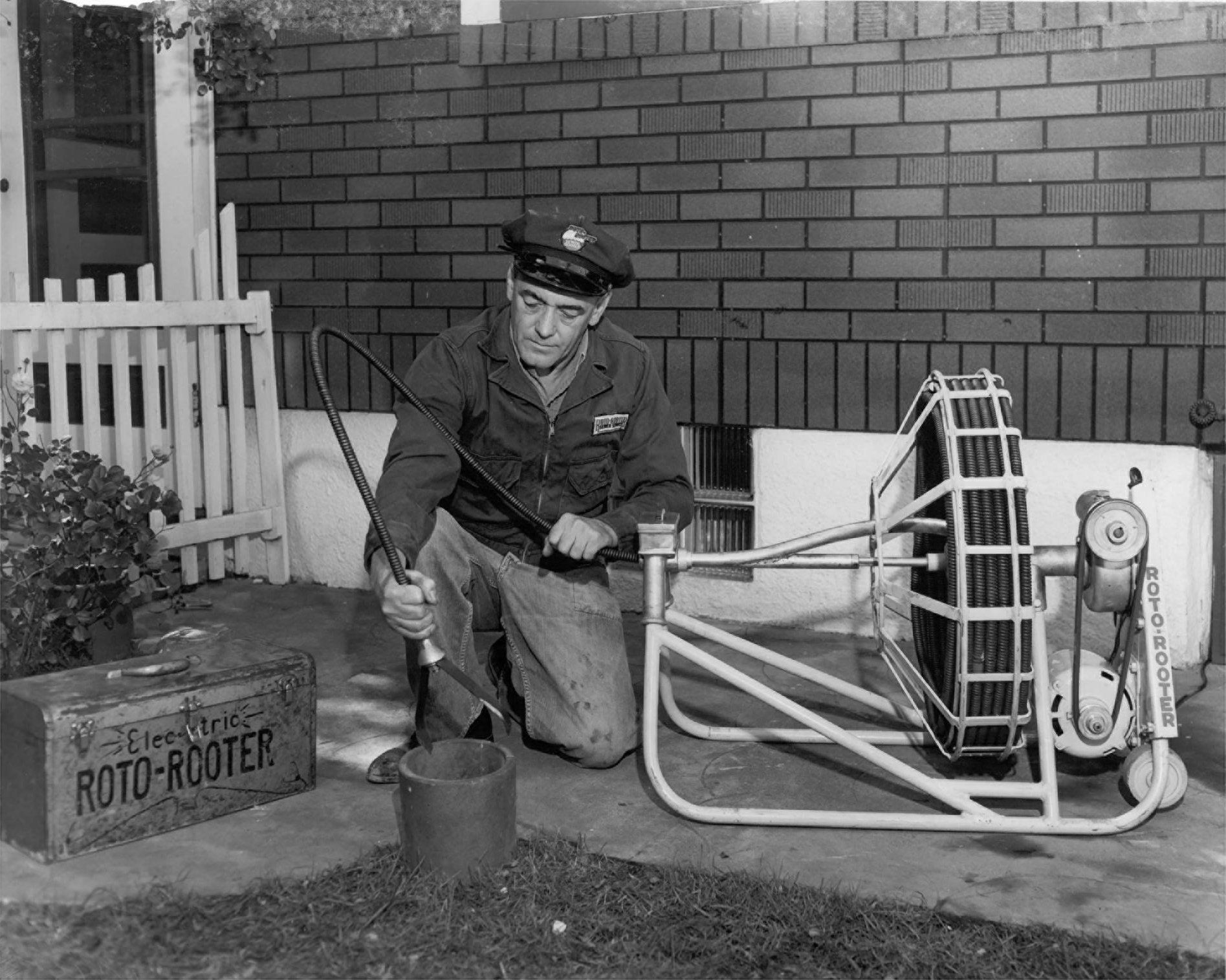 A man is kneeling down next to a box that says roto-rooter