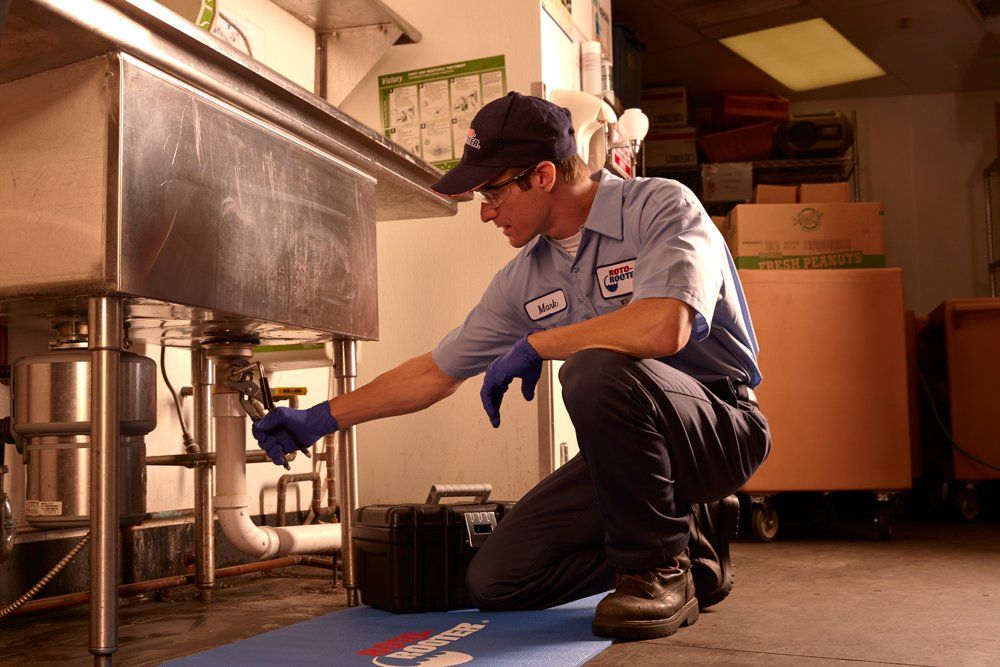 A man is kneeling down in a kitchen looking under a sink.