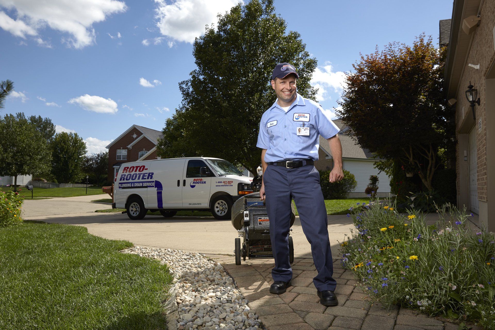 A man in a blue shirt is standing in front of a white van that says roto-rooter