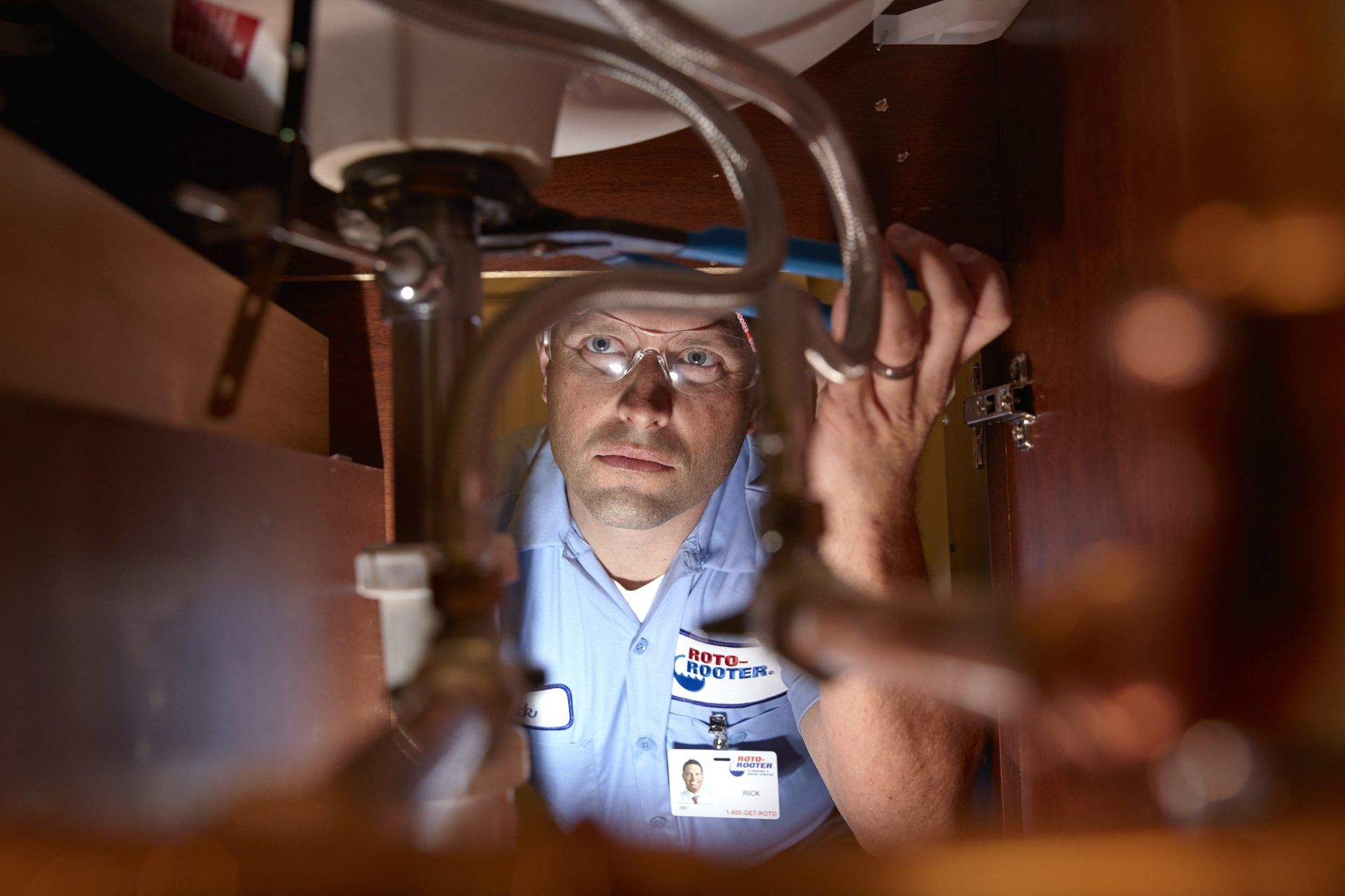A man is looking under a sink with a magnifying glass.