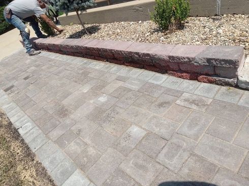 Worker installing a raised stone curb beside a paved walkway and planter bed