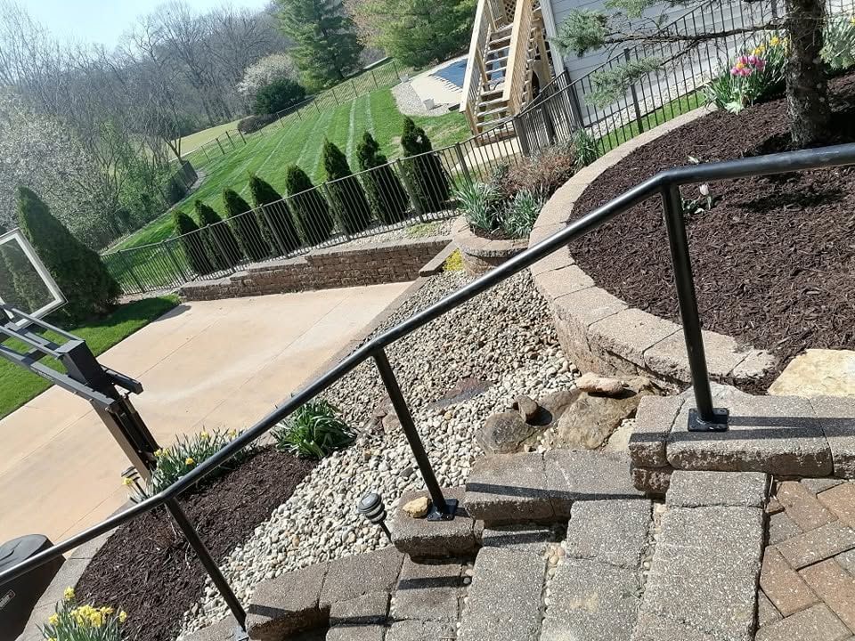 Steep outdoor steps with black railing leading to a landscaped garden and sidewalk below