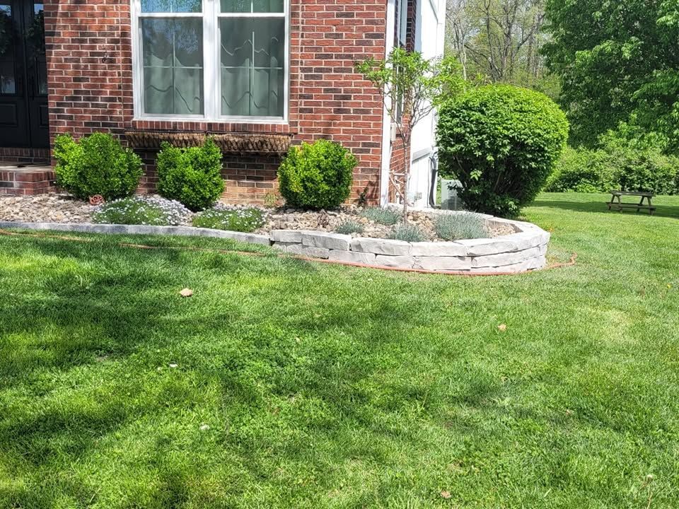 Brick house front yard with green lawn, shrubs, and a curved stone garden bed.