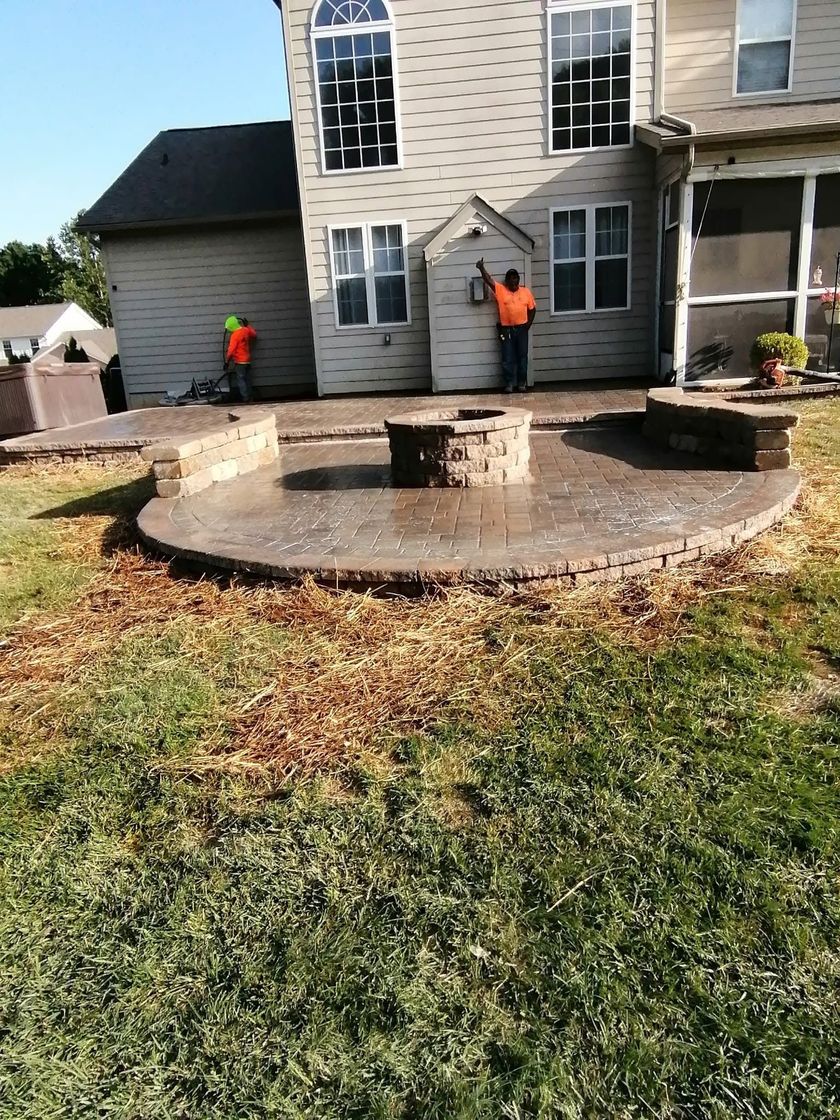Two workers in orange vests standing by a curved stone patio in front of a house
