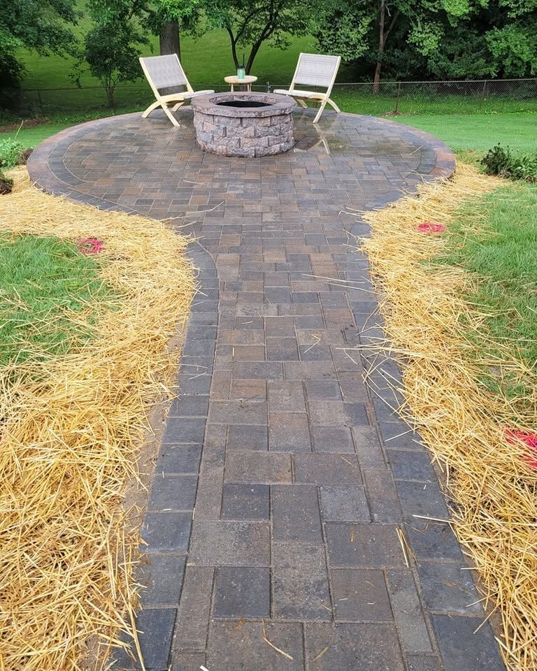 Stone patio walkway leading to a circular fire pit with two chairs in a grassy yard