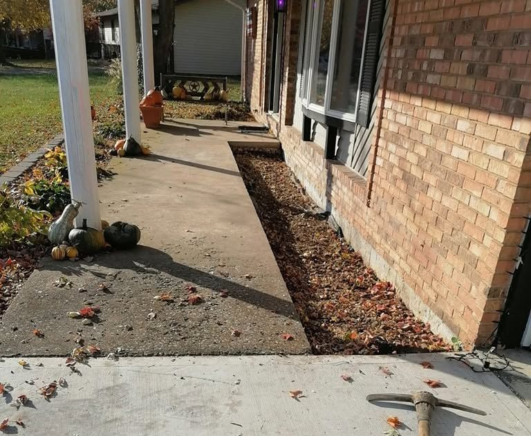 Front walkway beside a brick house, with pumpkins and fallen leaves along the path.