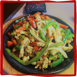 a black plate topped with chicken and vegetables on a wooden table .