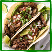 two tacos with meat , avocado , onions and limes on a plate .