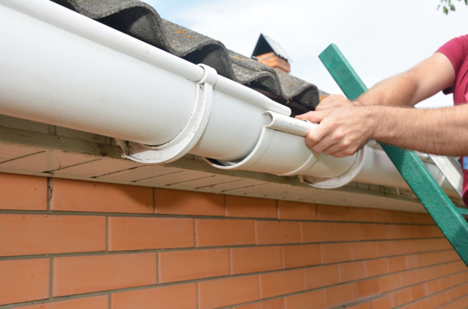 A Man Is Standing on A Ladder Fixing a Gutter on A Roof — Coffs Coast Plumbing in Korora, NSW