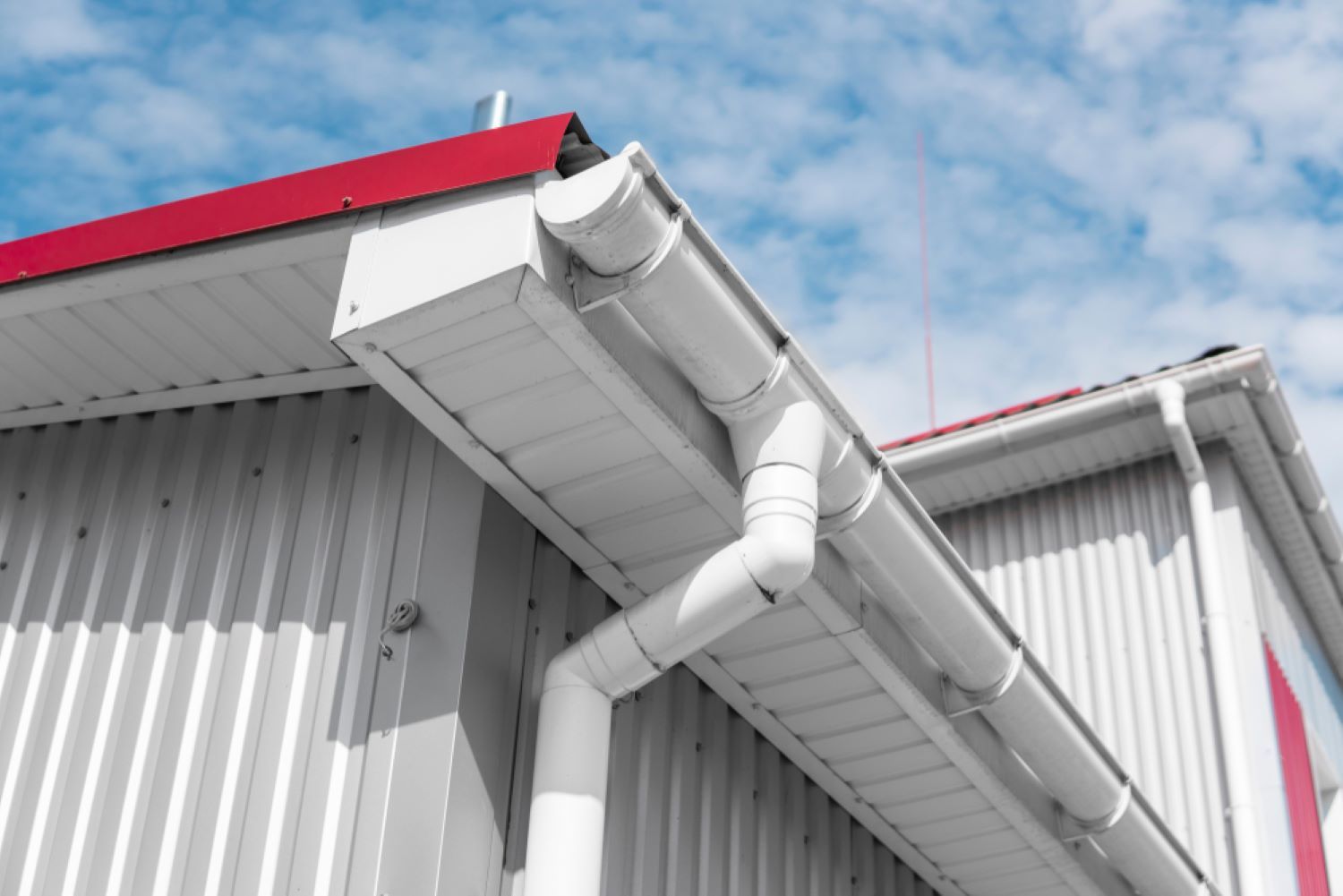 A White Gutter on The Side of A Building with A Red Roof — Coffs Coast Plumbing in Korora, NSW