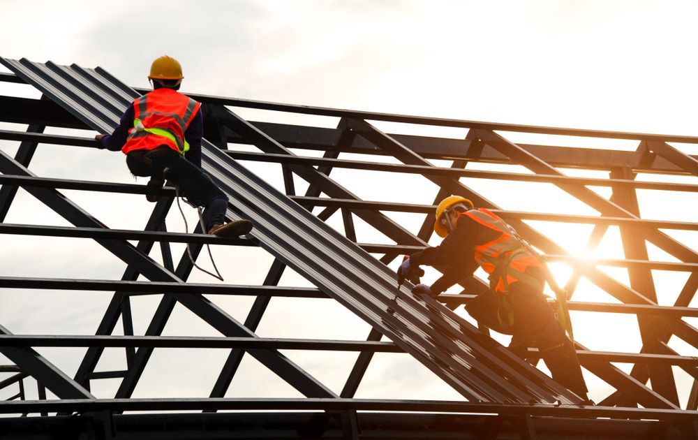Two Construction Workers Are Working on The Roof of A Building — Coffs Coast Plumbing in Korora, NSW