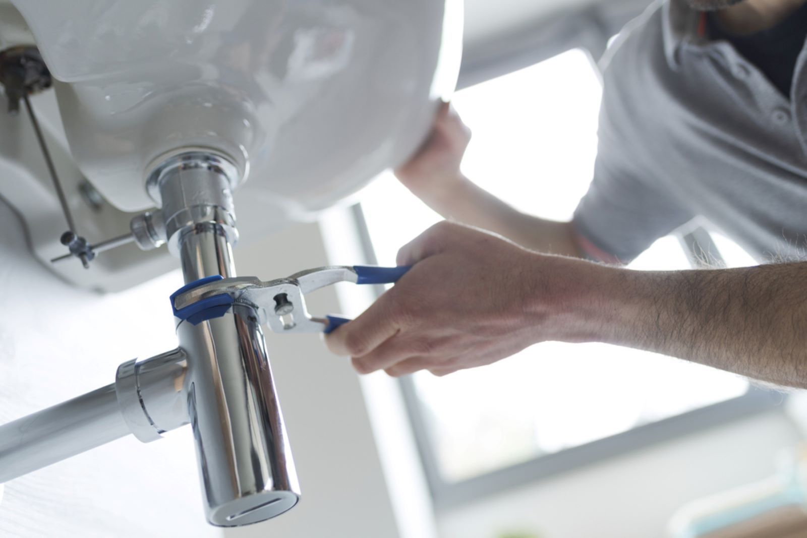 A Man Is Fixing a Sink with A Wrench — Coffs Coast Plumbing in Moonee Beach, NSW