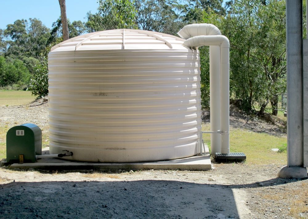 A Large White Water Tank Is Sitting Next to A Green Box — Coffs Coast Plumbing in Korora, NSW