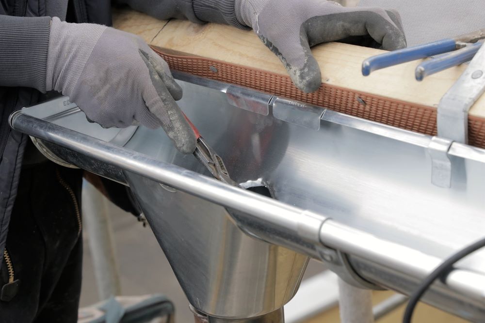 A Person Is Working on A Metal Gutter with A Pair of Pliers — Coffs Coast Plumbing in Korora, NSW