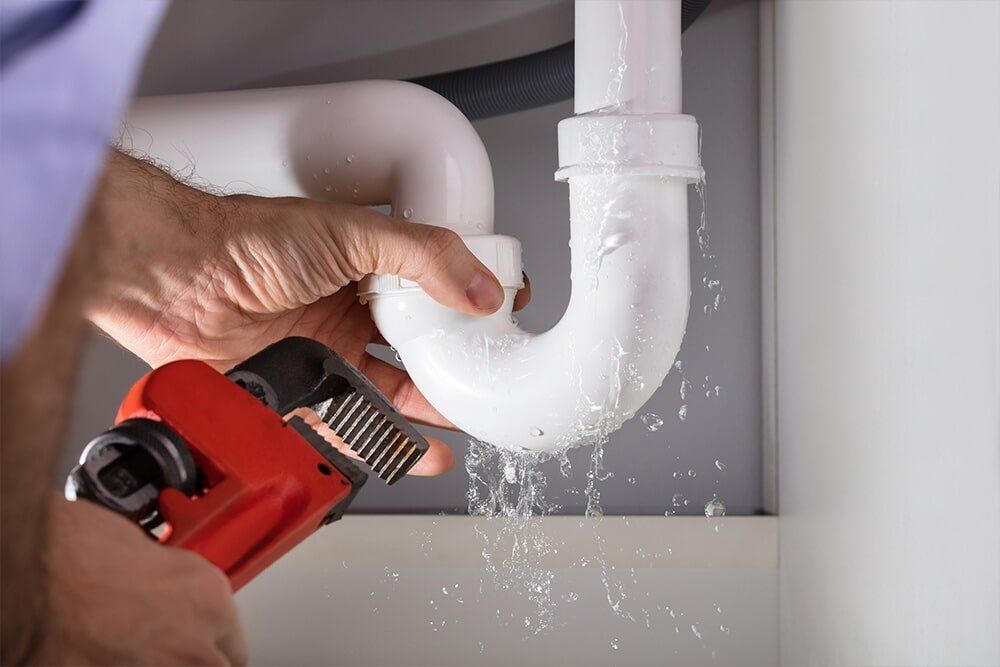 A Plumber is Fixing a Leaking Sink Pipe With a Wrench — Coffs Coast Plumbing in Korora, NSW