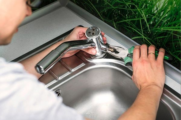 A Person is Fixing a Faucet in a Kitchen Sink — Coffs Coast Plumbing in Korora, NSW