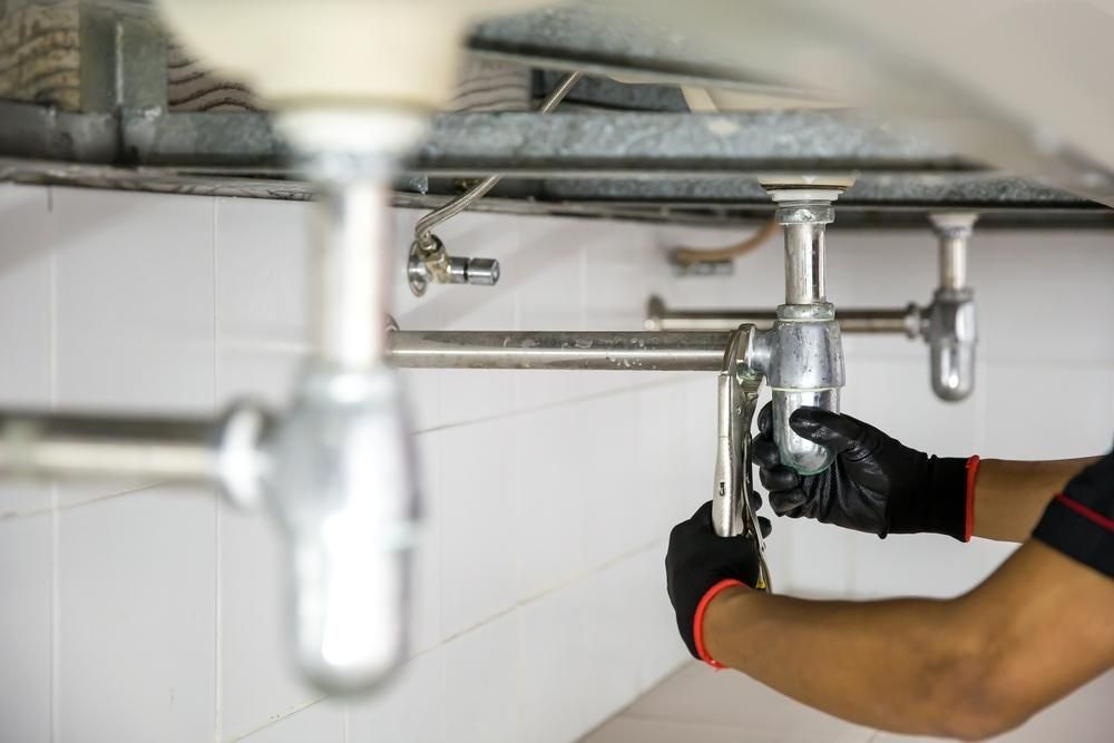 A Plumber Is Fixing a Sink Pipe in A Bathroom — Coffs Coast Plumbing in Korora, NSW