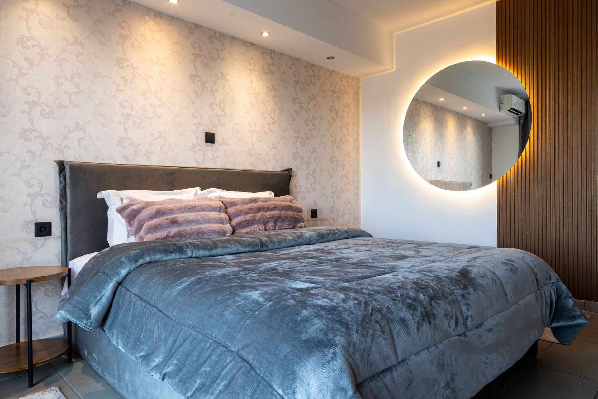 Modern bedroom with a large bed, gray bedding, round mirror, and wood-paneled accent wall