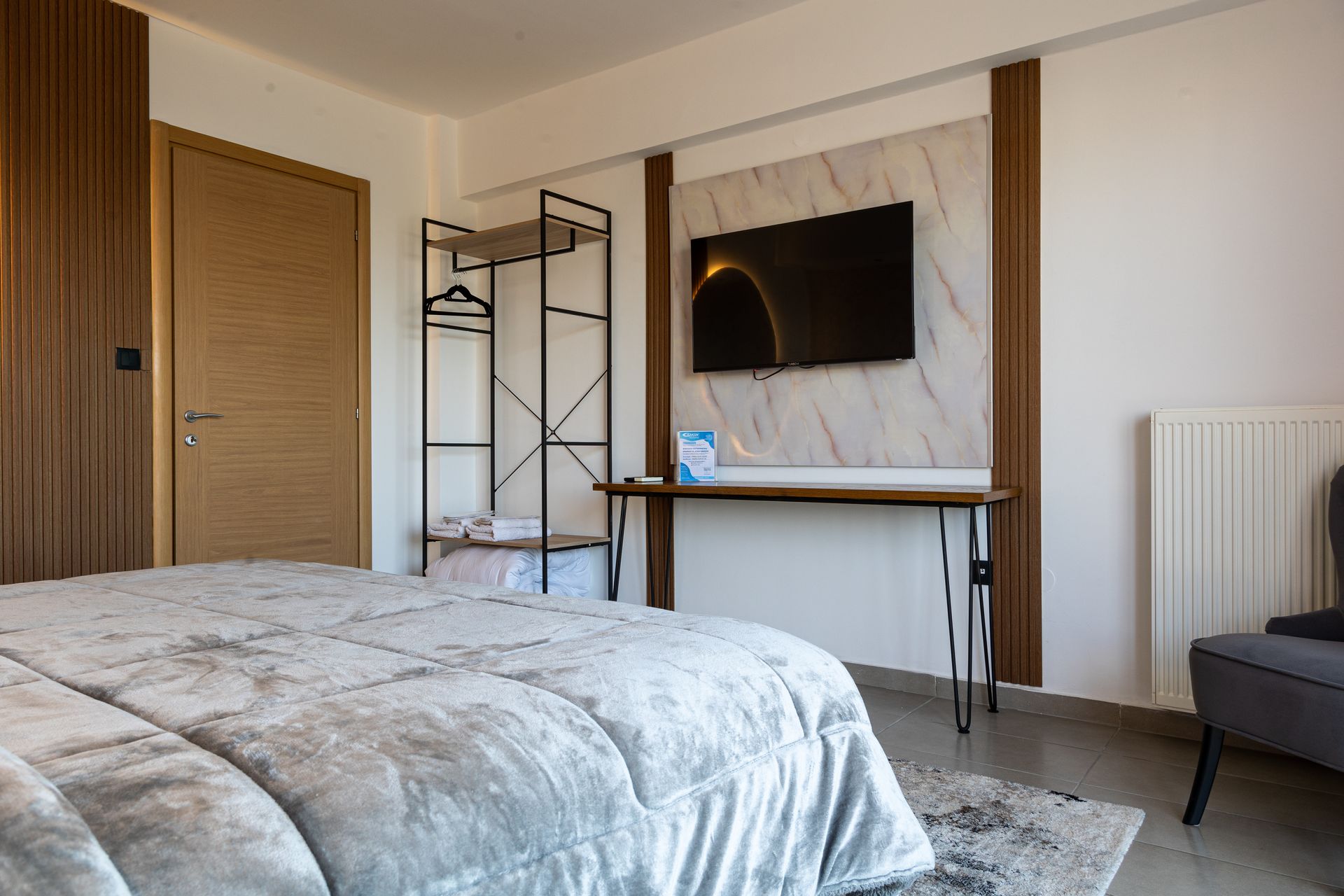 Modern bedroom with bed, wall-mounted TV, desk, wardrobe, and open clothing rack