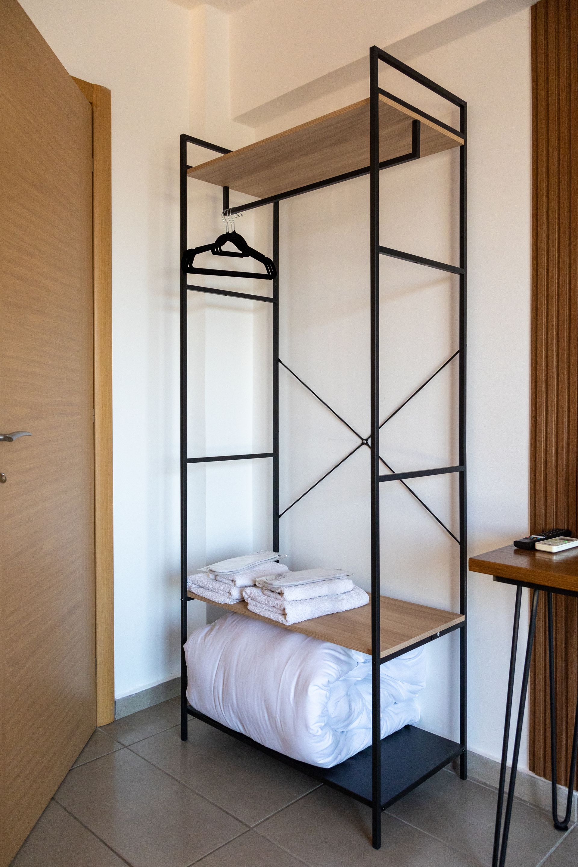 Minimal clothing rack with shelves and hanging space in a room, holding folded towels and a hanger.