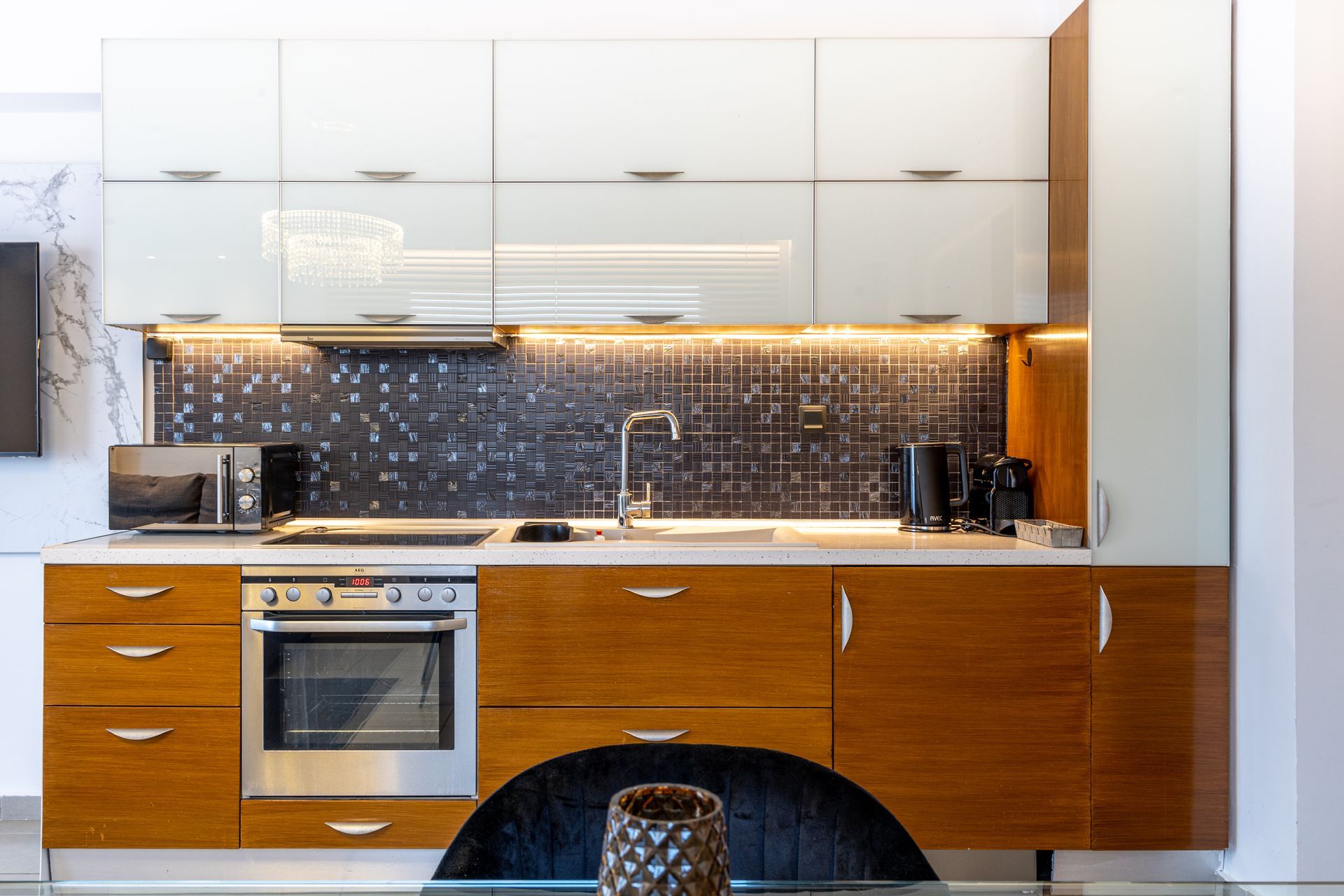 Modern kitchen with white upper cabinets, wood lower cabinets, stainless oven, and tiled backsplash under warm lighting