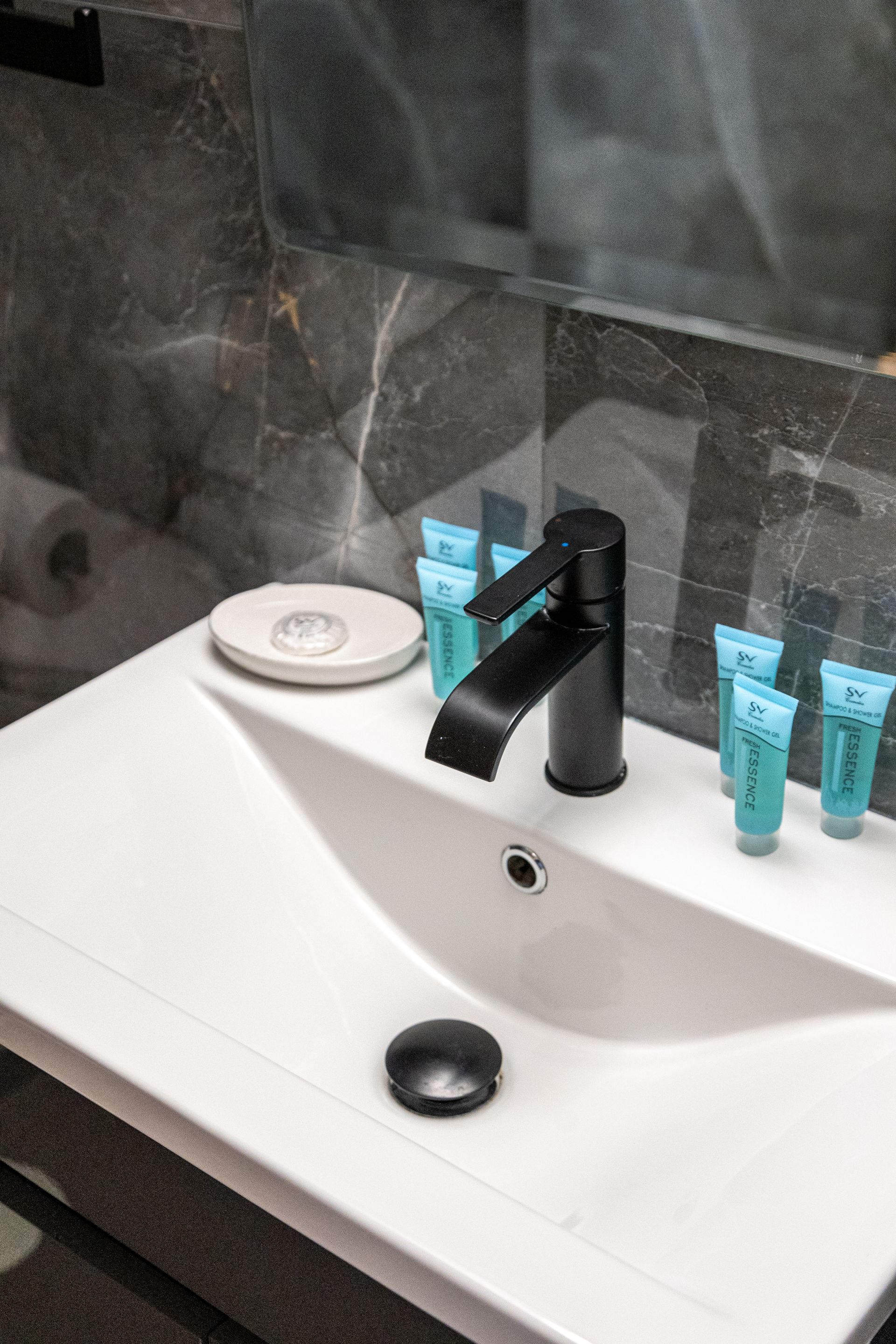 Modern bathroom sink with black faucet, soap dish, and blue toiletries on the counter