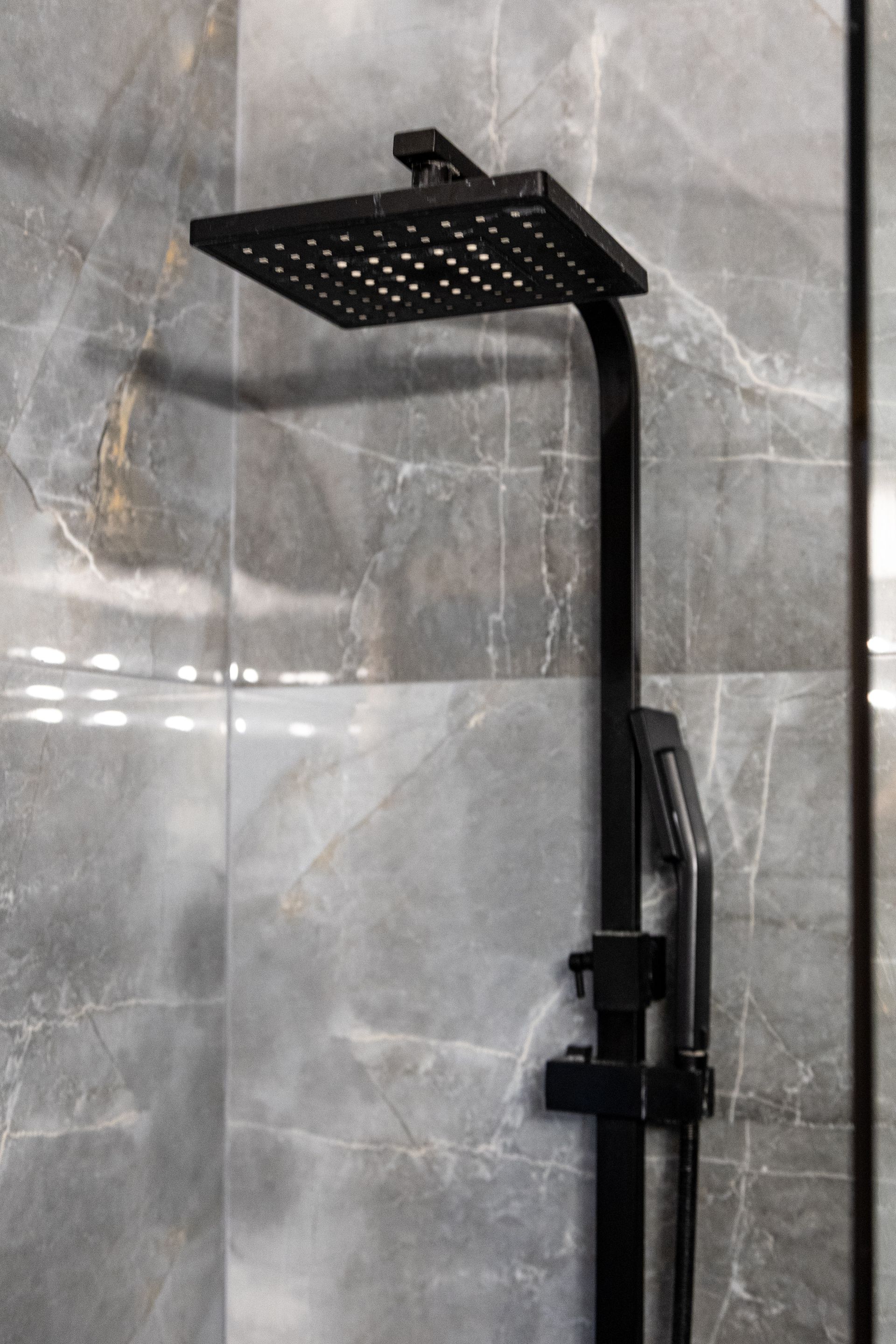 Black rainfall showerhead and handheld shower on gray tiled bathroom wall