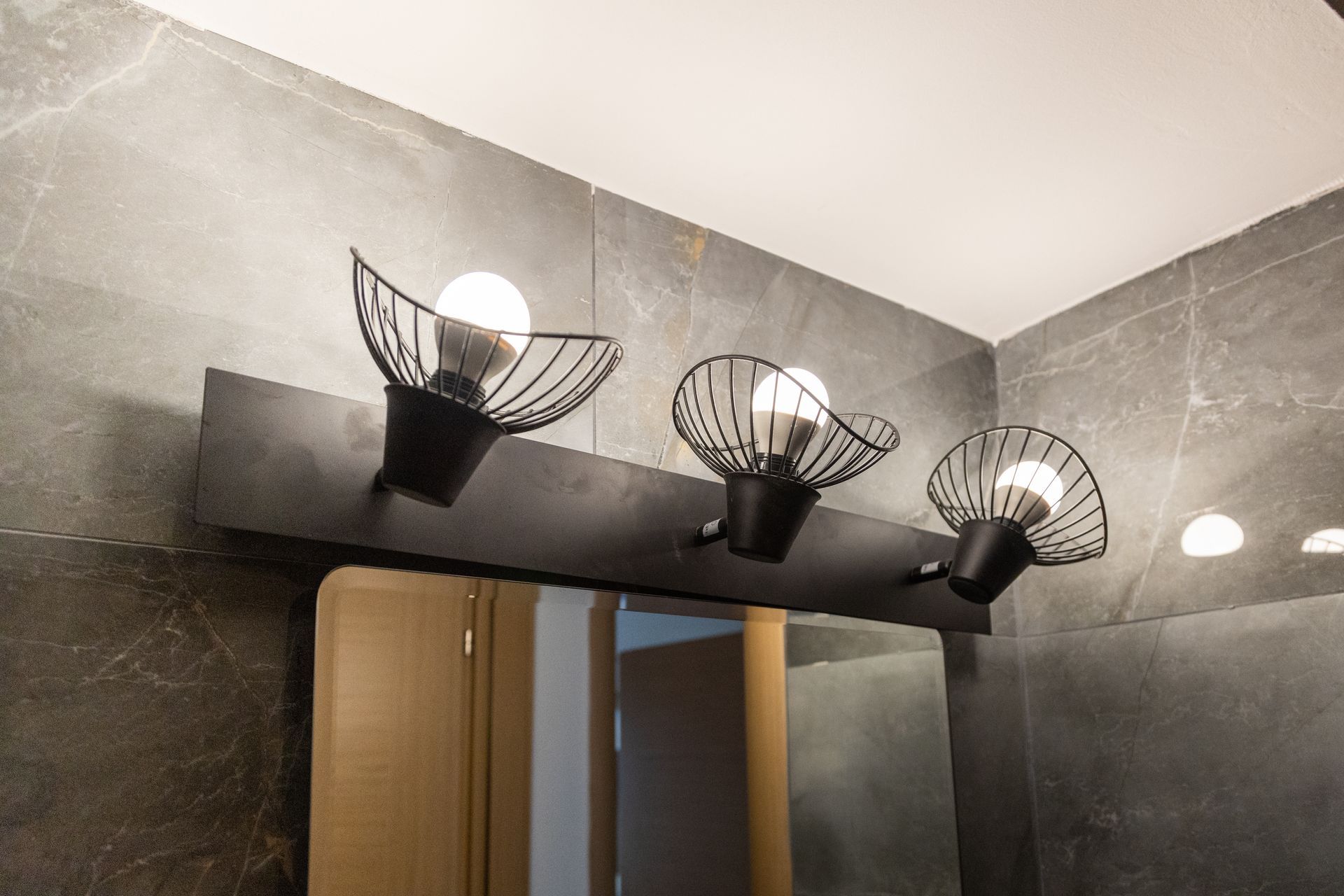 Modern bathroom vanity with three black bowl-shaped light fixtures above a mirror and sink area