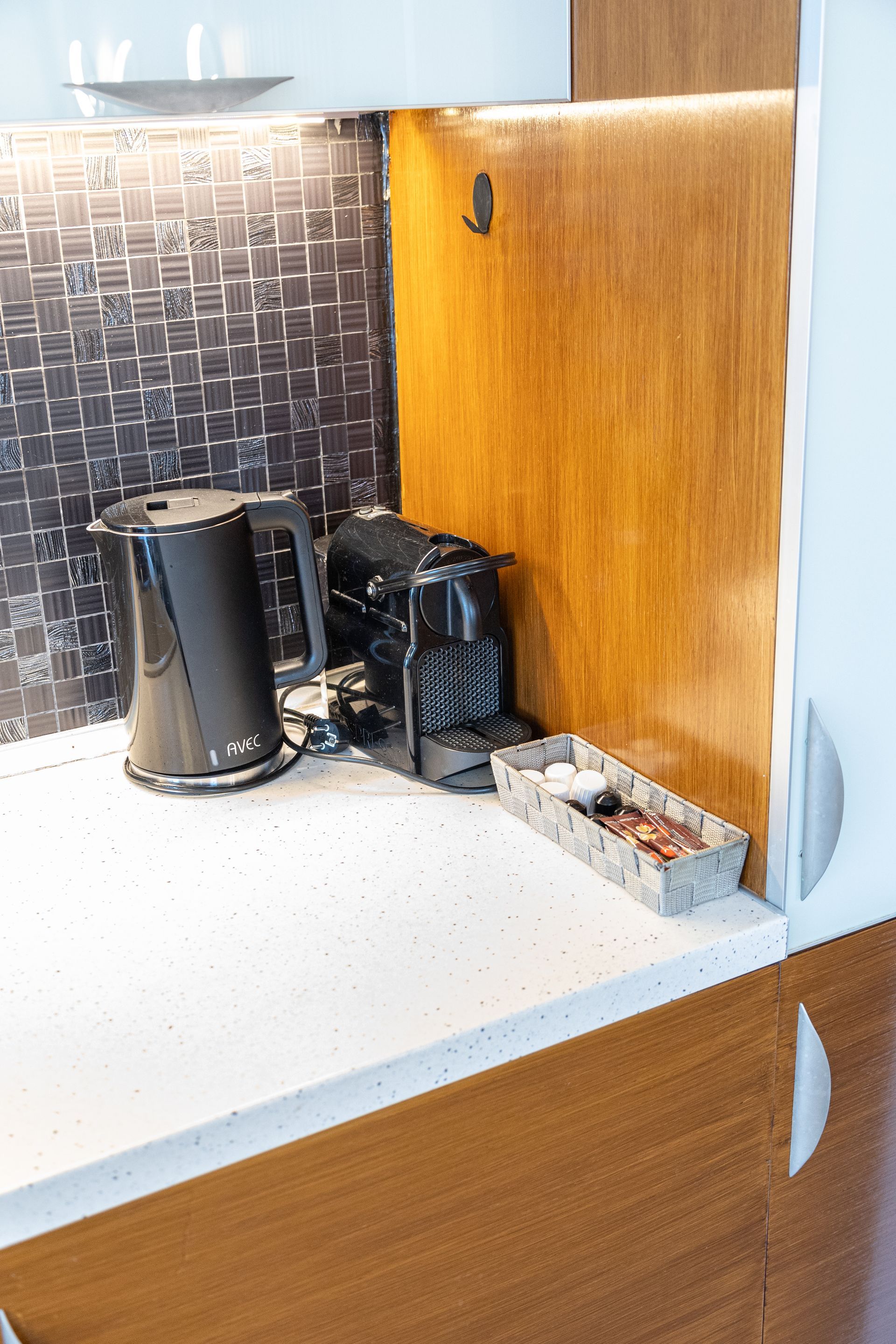 Kitchen counter nook with coffee maker, electric kettle, and power cords against wood paneling and tile backsplash