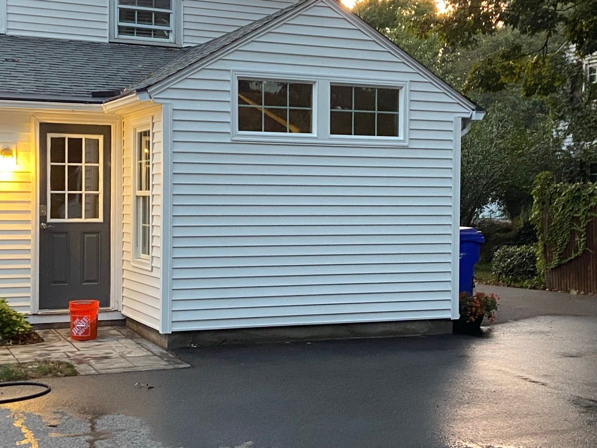 A white house exterior featuring a gray door, two small windows on the side wall, and a bright orange bucket on a patio.