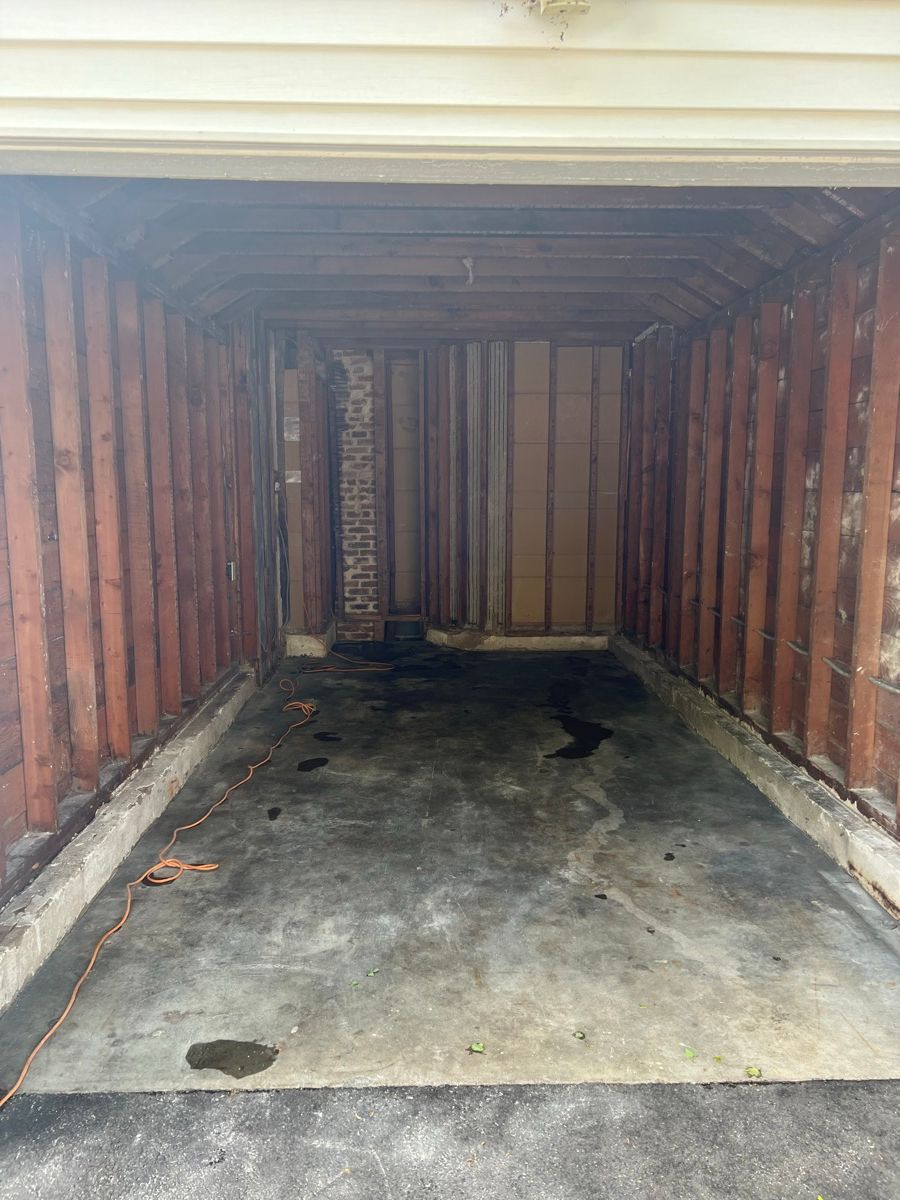 An open, empty garage interior with exposed wooden wall studs and a stained concrete floor.