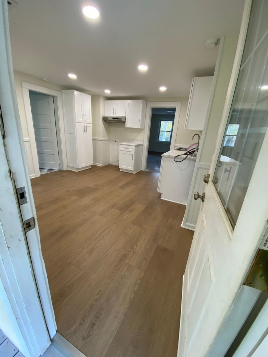 View of a renovated room with white cabinets, light wood flooring, and recessed lighting.