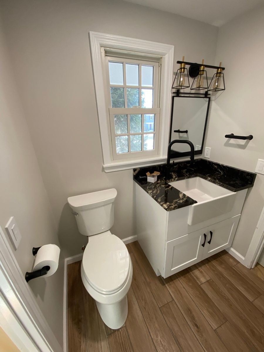 A small, modern bathroom featuring a white farmhouse sink with a black countertop, a toilet, and light gray walls.