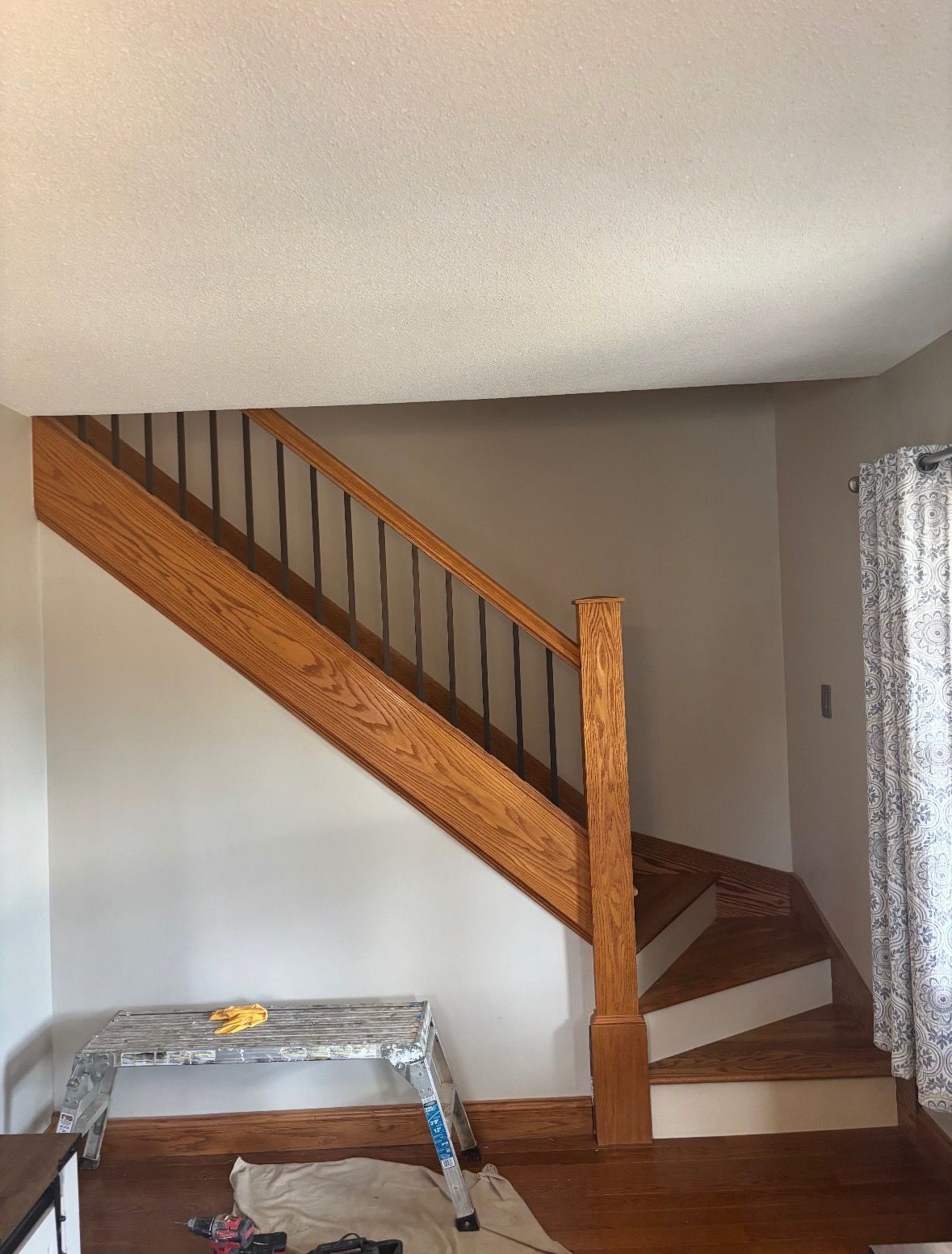 A staircase with wooden handrails and black metal balusters rises along a light-colored wall, with a work bench below.