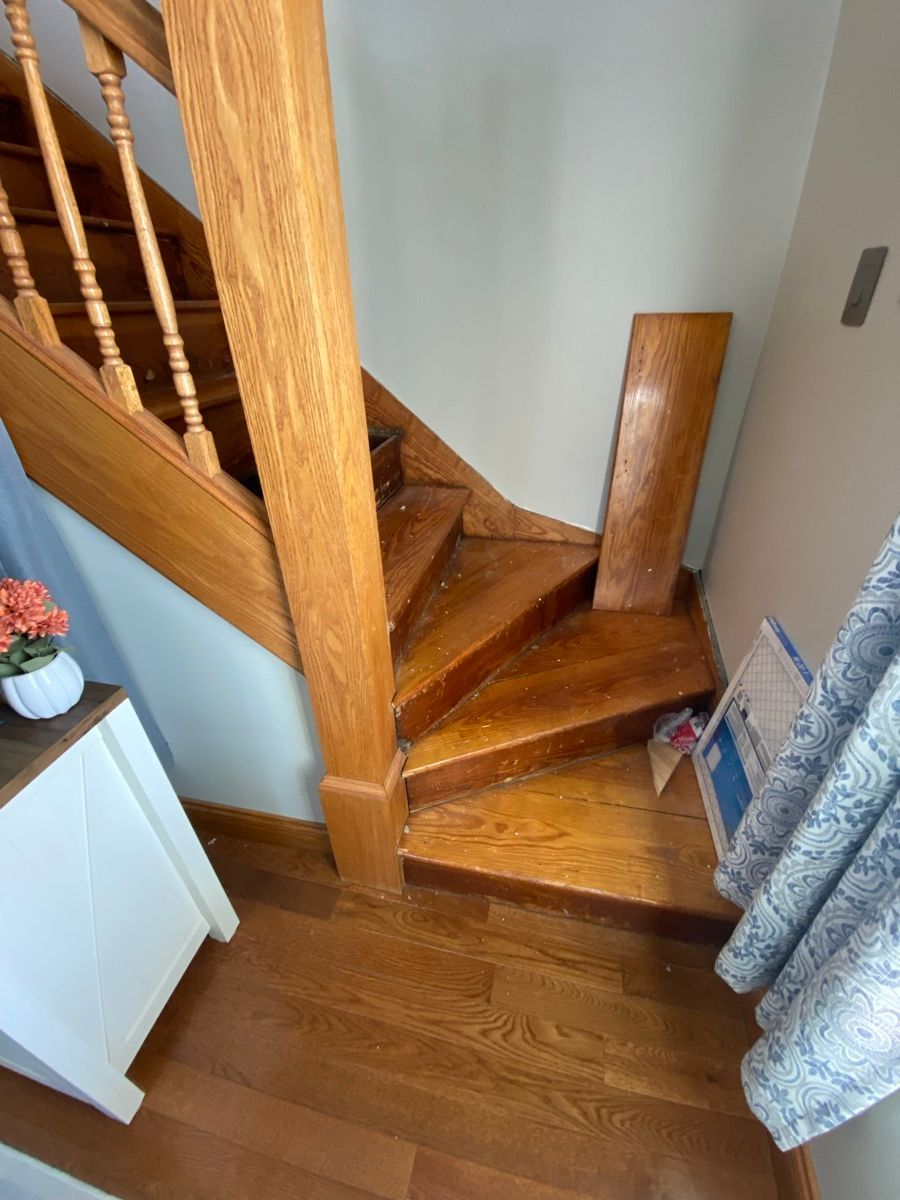 A wooden staircase features winder steps at the bottom, with a loose wooden board leaning against the wall nearby.