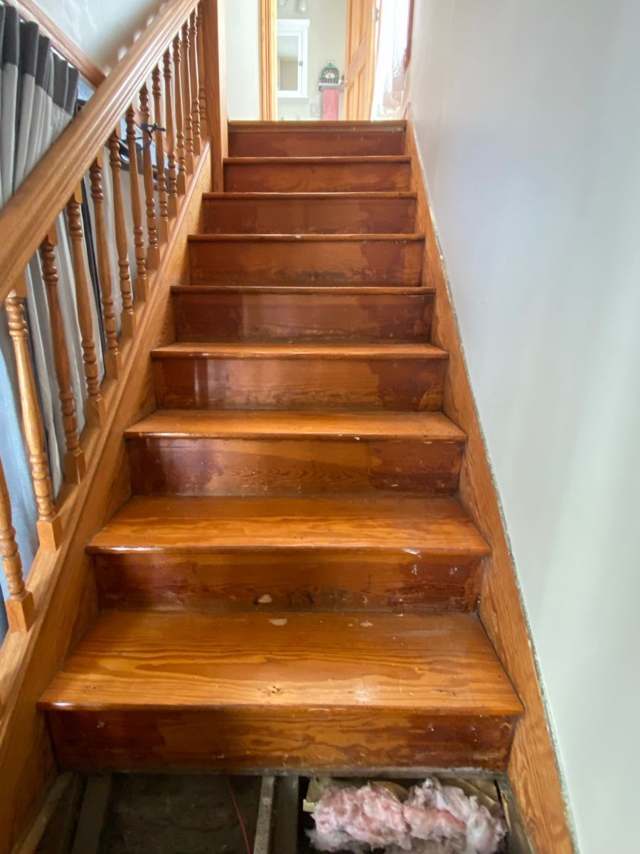 Wooden indoor staircase with a handrail, viewed from the bottom, with insulation visible under the bottom step.