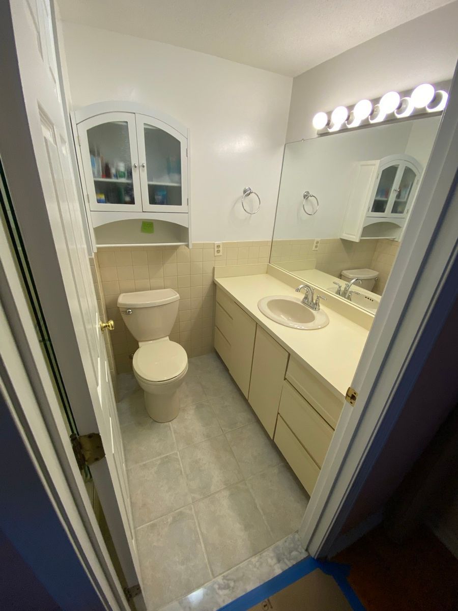 A bathroom with a toilet, vanity cabinet, large mirror, and wall-mounted storage cabinet, featuring light-toned finishes.
