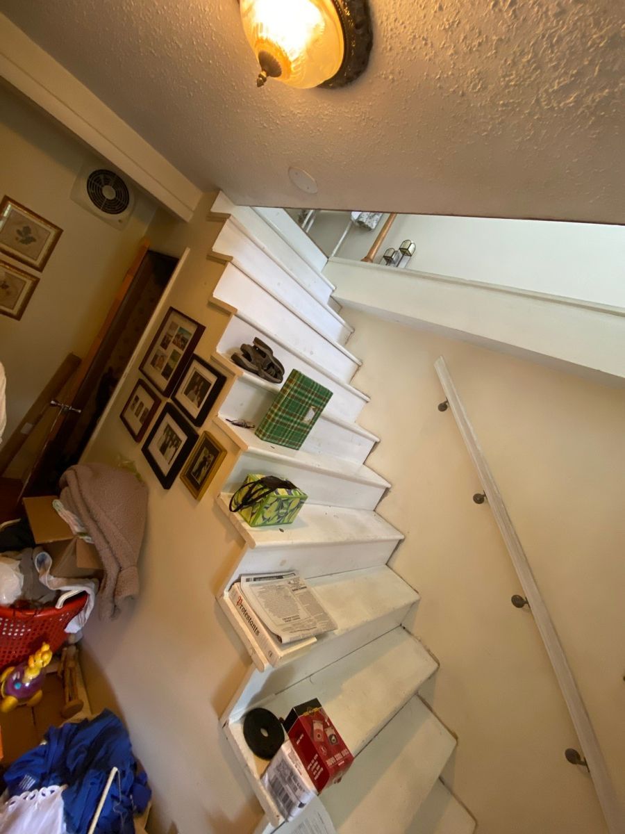 A set of white wooden stairs leading upward, decorated with several framed pictures on the adjacent wall.