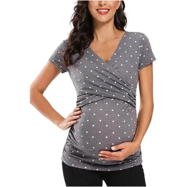 Mujer embarazada con blusa gris de lunares, sujetándose la barriga y sonriendo.