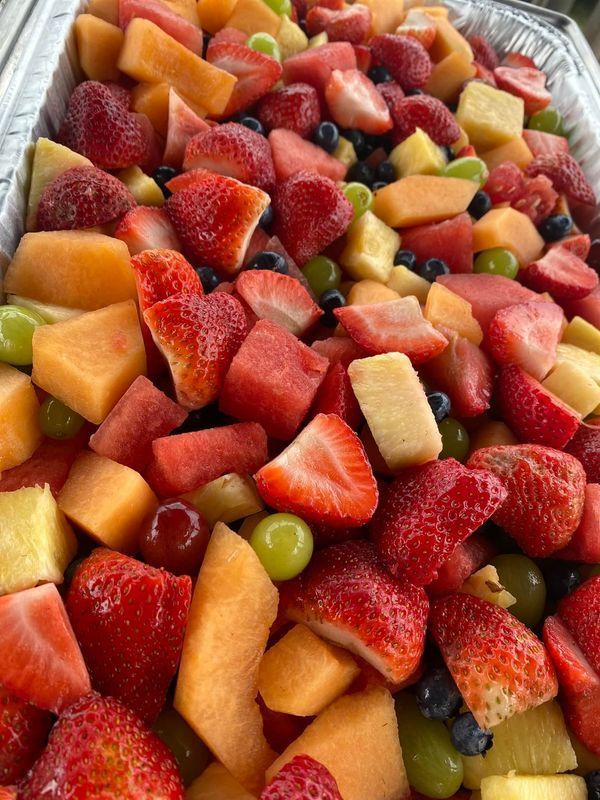 A metal tray filled with a fresh fruit salad containing strawberries, cantaloupe, pineapple, and green grapes.